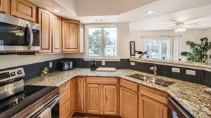A kitchen with wooden cabinets, a built-in microwave, a gas stove, granite countertops, a sink, and a ceiling fan. - Historic Westside Home: Central Location, AC & Game Room (Colorado Springs)