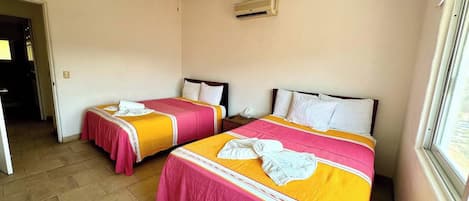 A hotel room with two beds, a ceiling fan, an air conditioning unit, and a window.