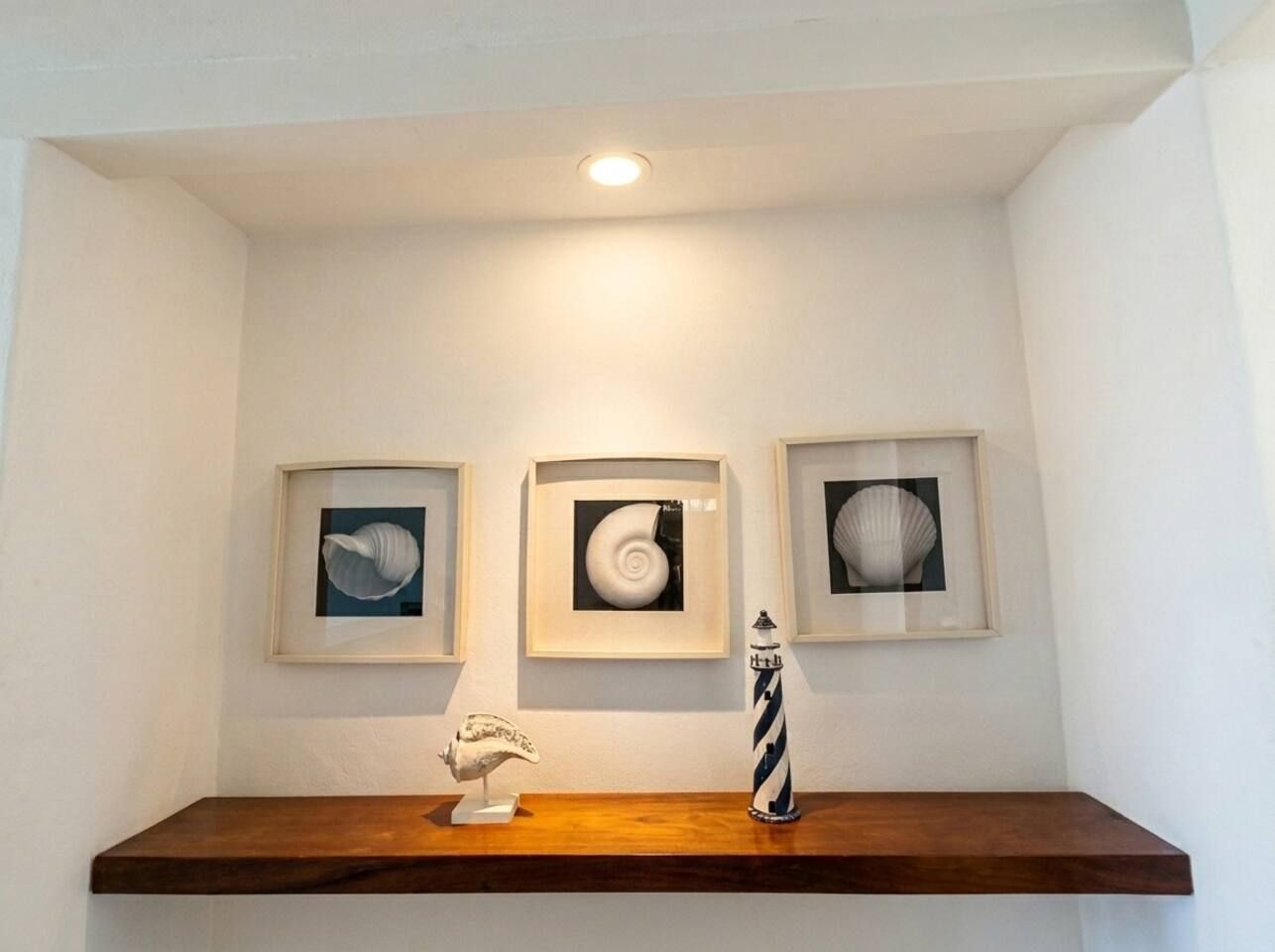 Un mur orné de trois œuvres d’art encadrées, d’une petite sculpture et d’une bouteille décorative posée sur une étagère en bois.