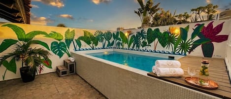 A swimming pool with a tiled edge, surrounded by potted plants and a wooden deck.
