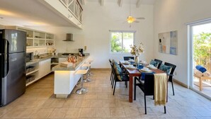Een moderne keuken met een centraal eiland, barkrukken en een eethoek met een tafel voor vier personen.