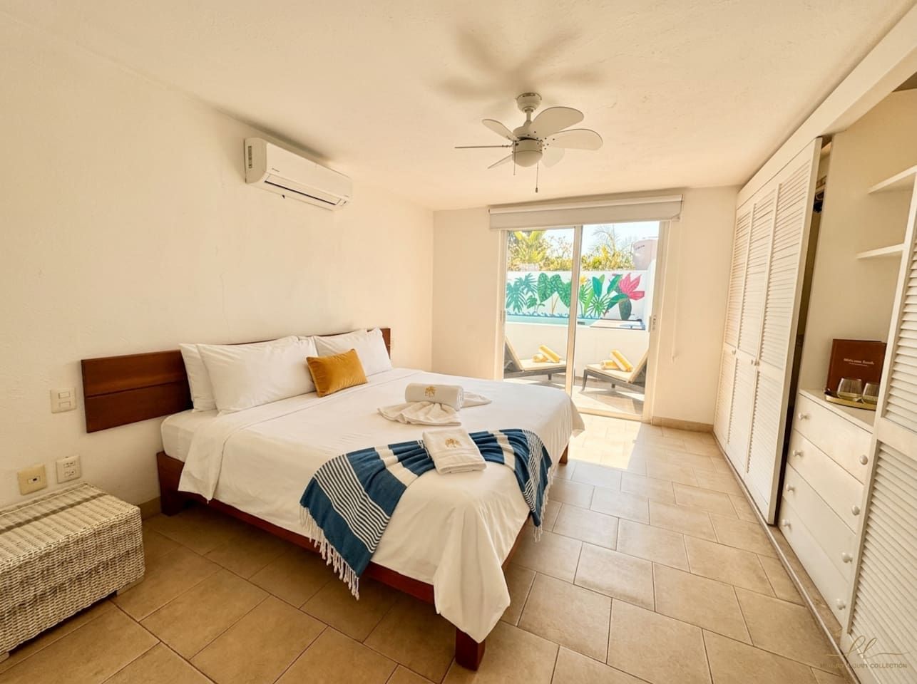 Une chambre d’hôtel équipée d’un lit, d’un ventilateur de plafond, d’un appareil de climatisation, d’une fenêtre donnant sur un espace verdoyant et d’un placard avec porte coulissante.