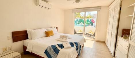 Une chambre d’hôtel équipée d’un lit, d’un ventilateur de plafond, d’un appareil de climatisation, d’une fenêtre donnant sur un espace verdoyant et d’un placard avec porte coulissante.