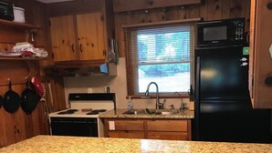 A kitchen with wooden cabinets, a granite countertop, a black refrigerator, and three stools with patterned seats.