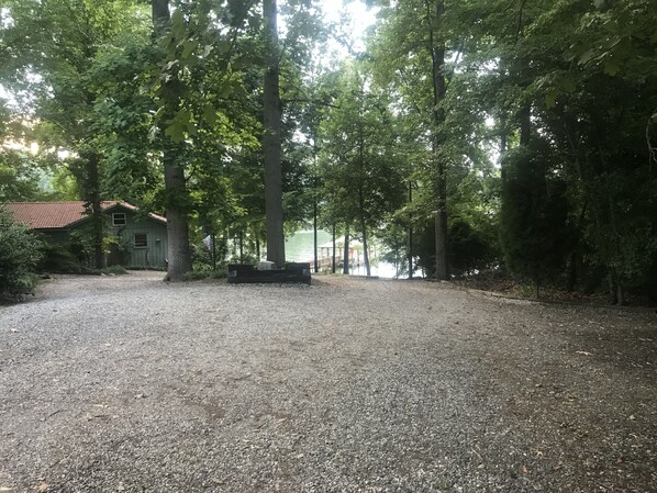 Ein Kiesweg führt zu einer hölzernen Bank in einem bewaldeten Gebiet, im Hintergrund ist ein Haus zu sehen.
