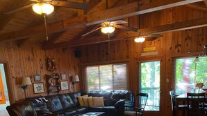 A cozy cabin interior with a wooden ceiling, a black leather couch, a dining area, and a granite countertop.