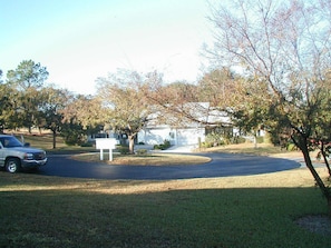 driveway leads to a charming home surrounded by a lush lawn and trees.