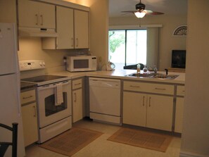 Compact kitchen with microwave, stove, oven, and dishwasher, featuring a window and ceiling fan.