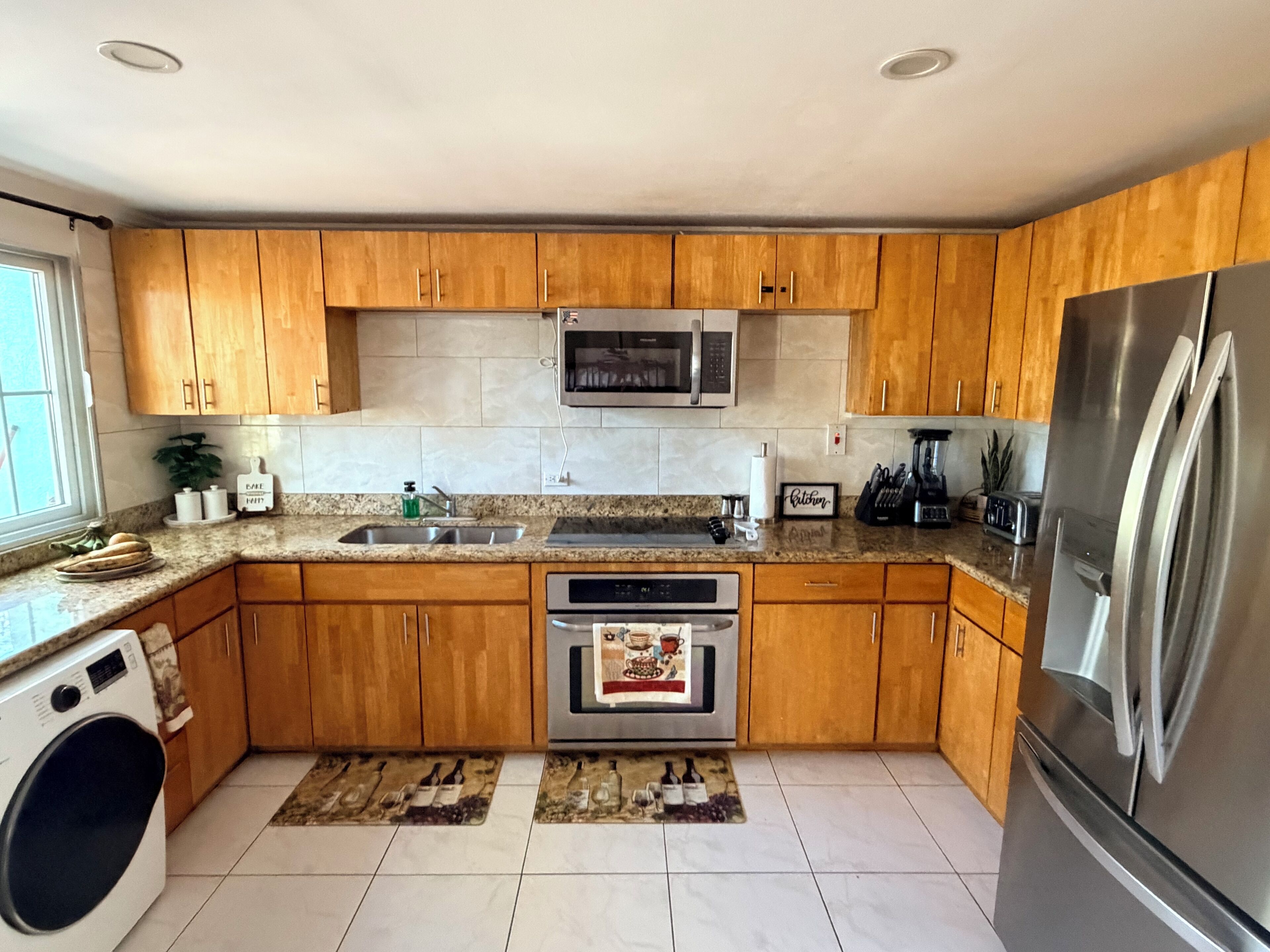A kitchen with wooden cabinets, a stainless steel refrigerator, a microwave, a dishwasher, and a washing machine.