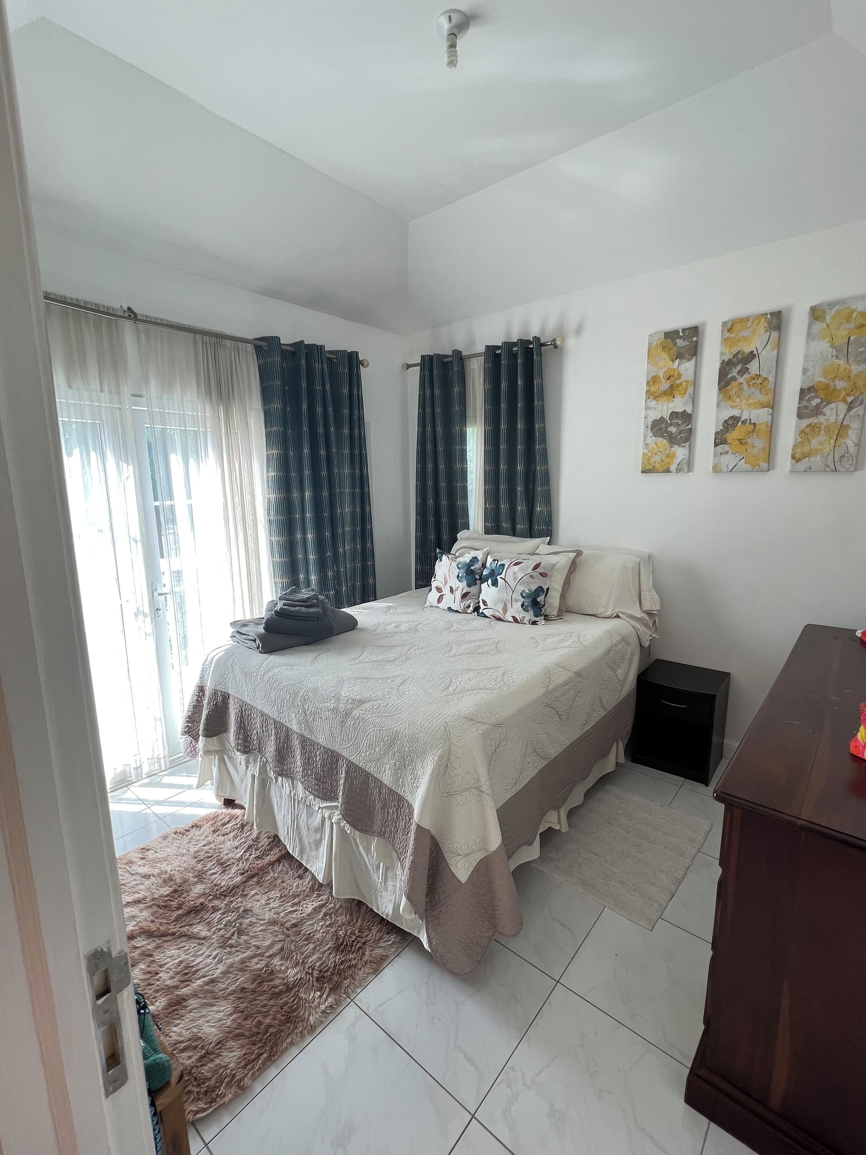 Une chambre à coucher avec un lit, des rideaux, une table de chevet, une commode et des œuvres d’art accrochées au mur.