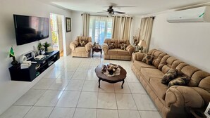 A living room with a flat-screen TV, two sofas, a coffee table, and a ceiling fan. - CHARMING 2 BEDROOM HOME: 3 BEDS, SLEEPS 1-5, 24hr SECURITY, PRIVATE POOL & BEACH (Negril)