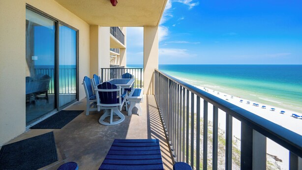 A balcony with a table and chairs, overlooking a beach with umbrellas. - Beautiful 2BR Gulf Front Condo - Phoenix V 1106 (Orange Beach)