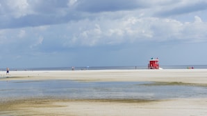 En strand med ett badvakts torn, en sandstrand och ett lugnt hav.