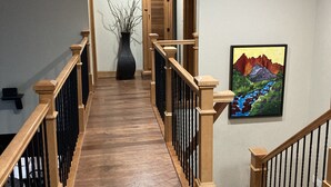 Eine Holztreppe mit schwarzen Geländern führt zu einer Empore. Auf der Empore steht eine große Vase mit Zweigen.