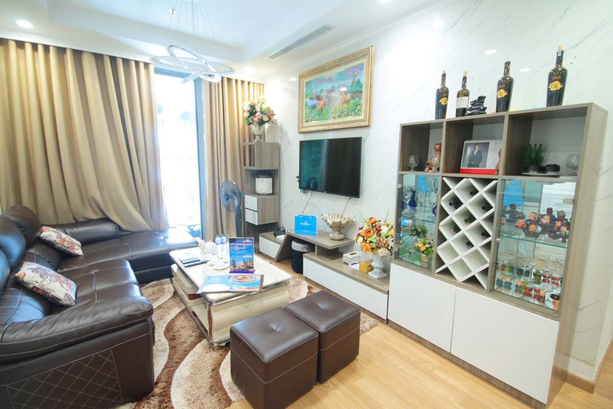 A modern living room with a leather sofa, a coffee table, and a TV mounted on the wall. There is a glass cabinet with decorative items and a painting above it.