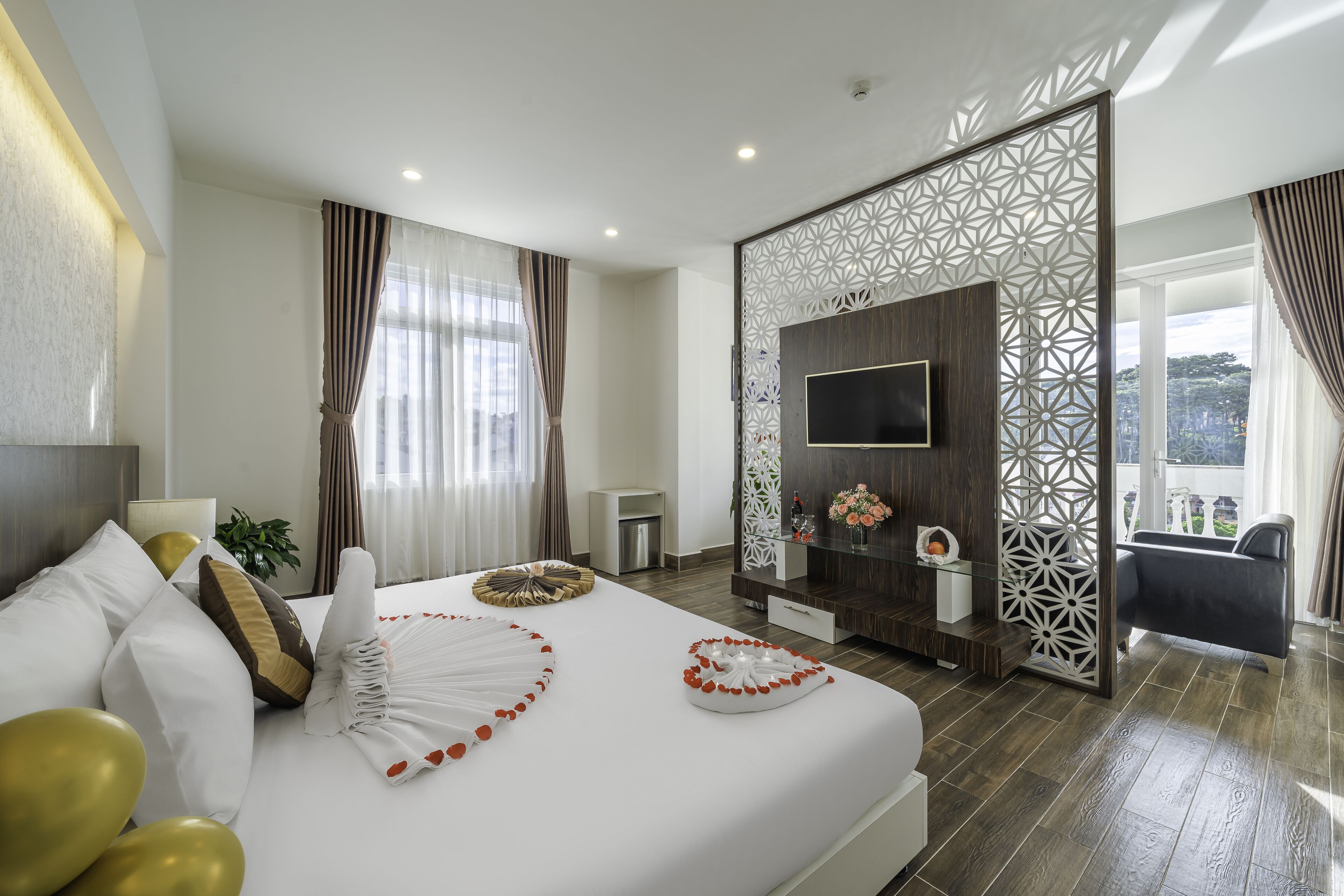 A modern hotel room with a large bed, a TV mounted on a wooden panel, and a balcony with a view.