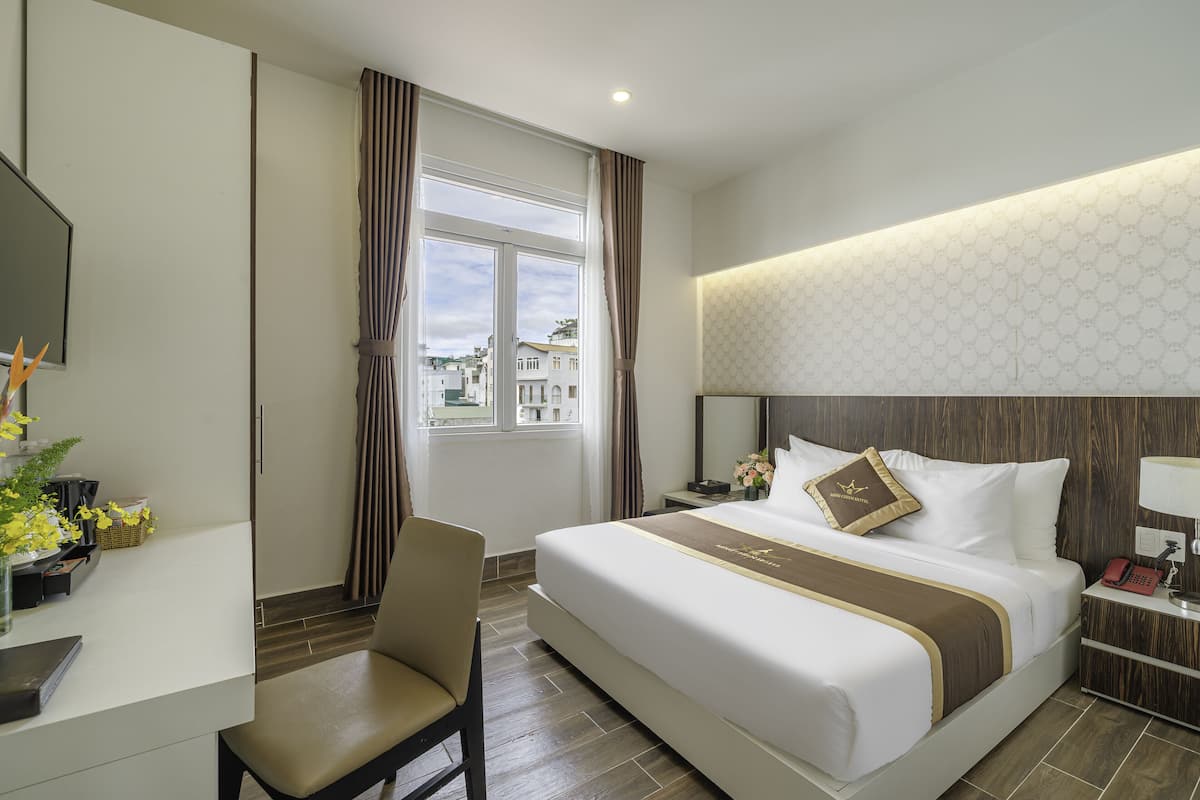 Une chambre d’hôtel avec un grand lit, un bureau avec une chaise, une table de chevet et une vue sur les bâtiments à travers la fenêtre.