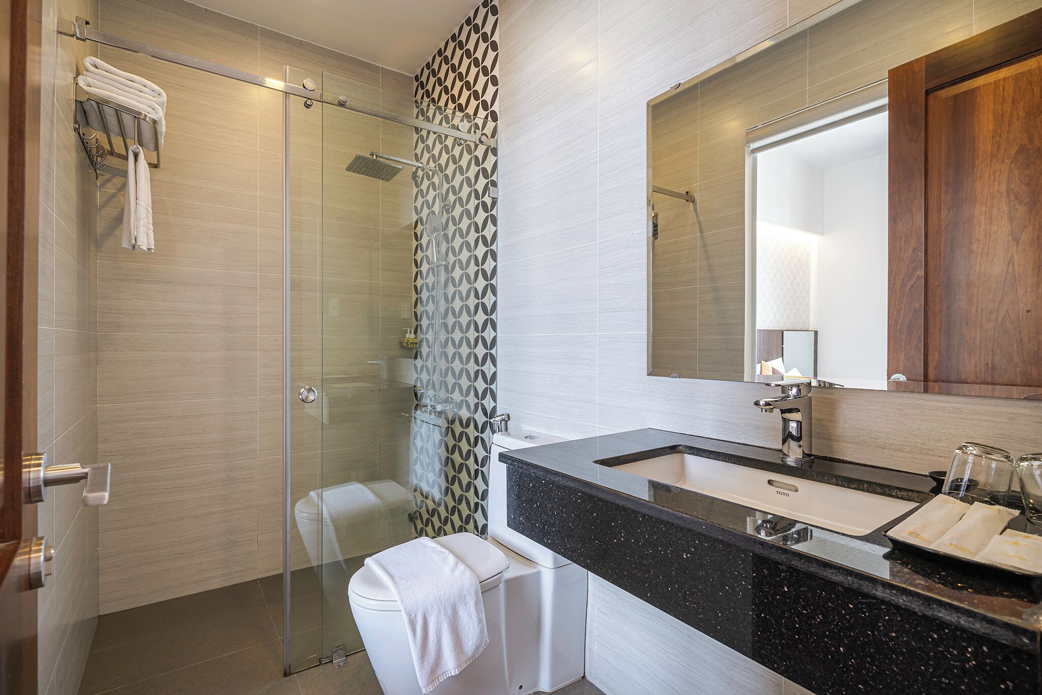 A modern bathroom with a glass shower enclosure, a black granite sink, and a large mirror.