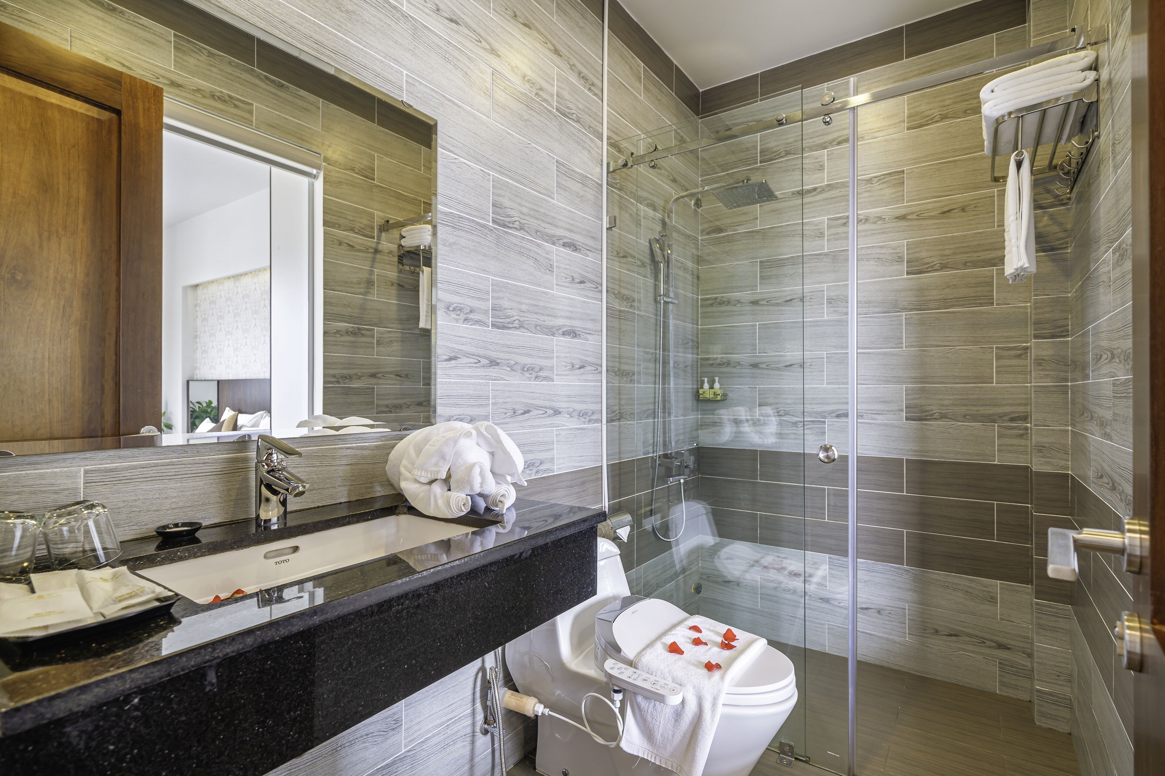 A modern bathroom with a black countertop, a glass shower enclosure, and a wooden vanity.