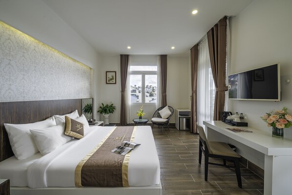 A hotel room with a large bed, a desk, a chair, a TV, and a window with curtains. - Minh Chien Hotel (Xuan Huong - Da Lat)