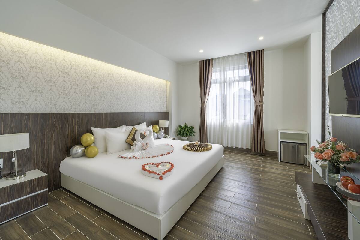 Une chambre d’hôtel moderne avec un grand lit, une table de chevet avec une lampe, une petite plante et un miroir au mur.
