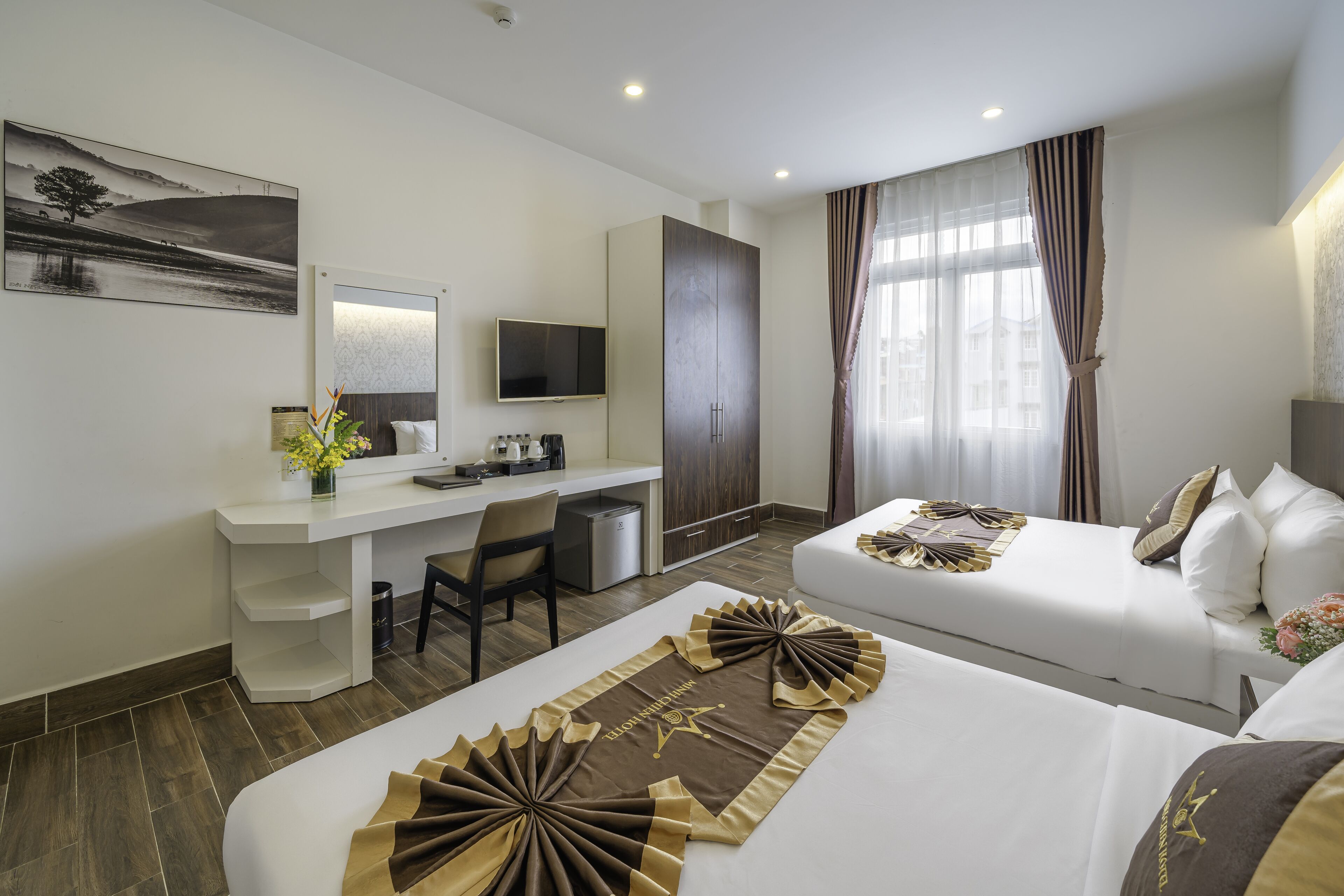 Quarto de hotel com escrivaninha, televisão, cama com almofadas decorativas e janela com cortinas.