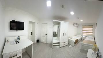 A modern bedroom with a white wardrobe, a bed with a beige headboard, a bedside table, and a flat-screen TV mounted on the wall.