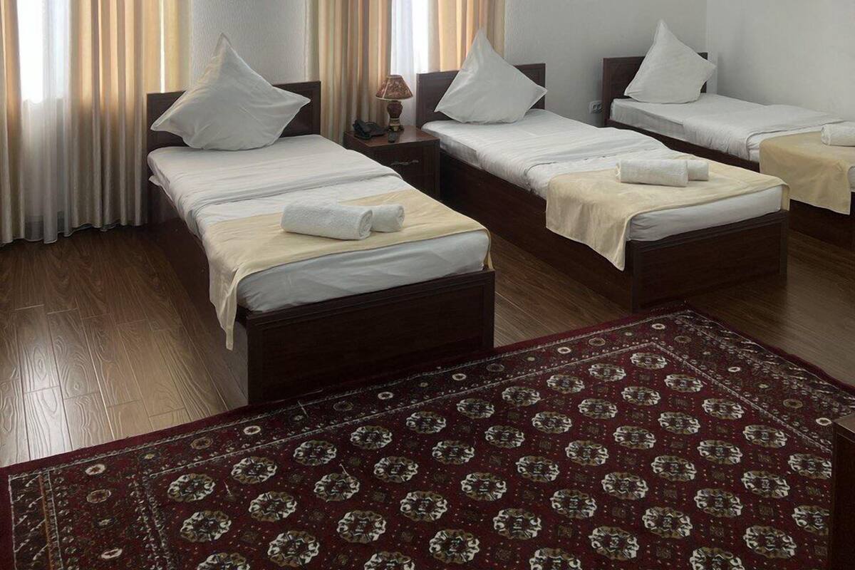 A hotel room with two single beds, a large bed, and a carpeted floor.