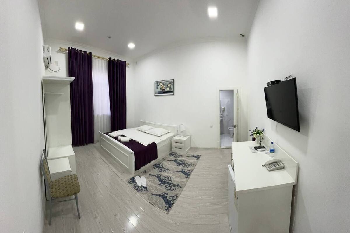 A modern hotel room with a bed, a desk, a chair, a TV, and a bathroom door.