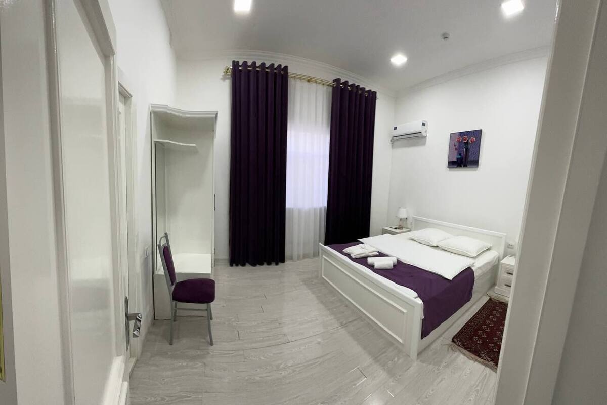 A bedroom with a bed, a chair, a wardrobe, and a window with curtains.