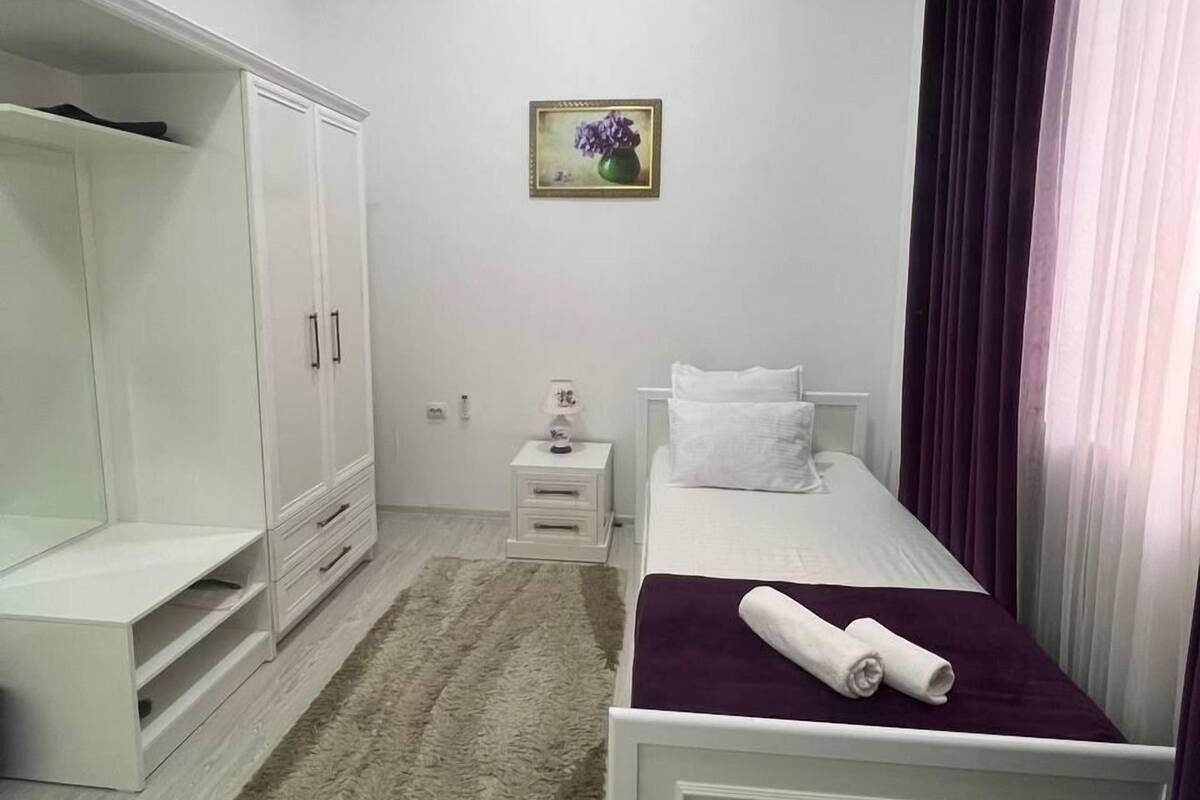 A bedroom with a bed, a wardrobe, a nightstand, a lamp, and a painting on the wall.
