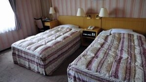 Una habitació d'hotel amb dos llits, cadascun amb roba de llit a ratlles, una tauleta de nit amb una làmpada i una fotografia encadrada a la paret.