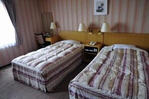 Habitación de hotel con dos camas, cada una con ropa de cama a rayas, una mesita de noche con lámpara y un cuadro en la pared.