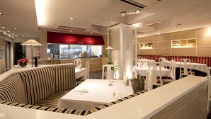 Un moderno vestíbulo de hotel con mostrador de recepción, zona de estar y un restaurante al fondo.