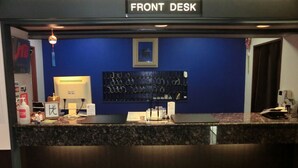 Un área de recepción con un mostrador oscuro, un monitor de computadora, un teléfono y una pantalla montada en la pared.