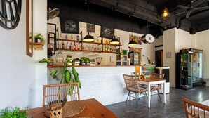 A restaurant interior with a white brick wall, wooden tables and chairs, and a bar area with shelves of bottles and glasses. - Kata Station (Karon)