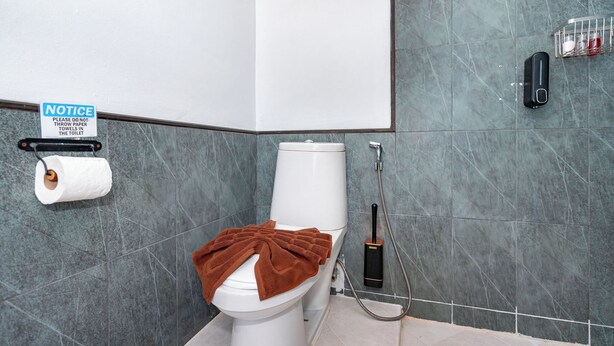 Un baño con un inodoro, dispensador de toallas de papel, un letrero informativo y un secador de manos.