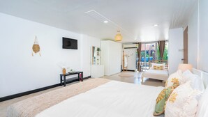 A modern hotel room with a large bed, a flat-screen TV, a small table with a lamp, and a view of the outdoor balcony. - Kata Station (Karon)