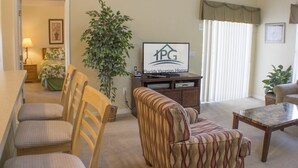 Un salon avec un canapé, des fauteuils, une table basse, un téléviseur et une plante.