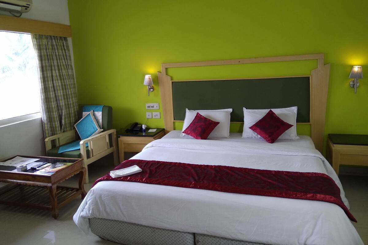 Een hotelkamer met een groot bed, een houten hoofdeinde, een bureau met stoel, een nachtkastje en een raam met gordijnen.