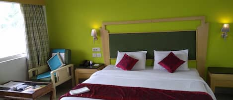 Habitación de hotel con una cama grande, cabecero de madera, escritorio con silla, mesita de noche y ventana con cortinas.