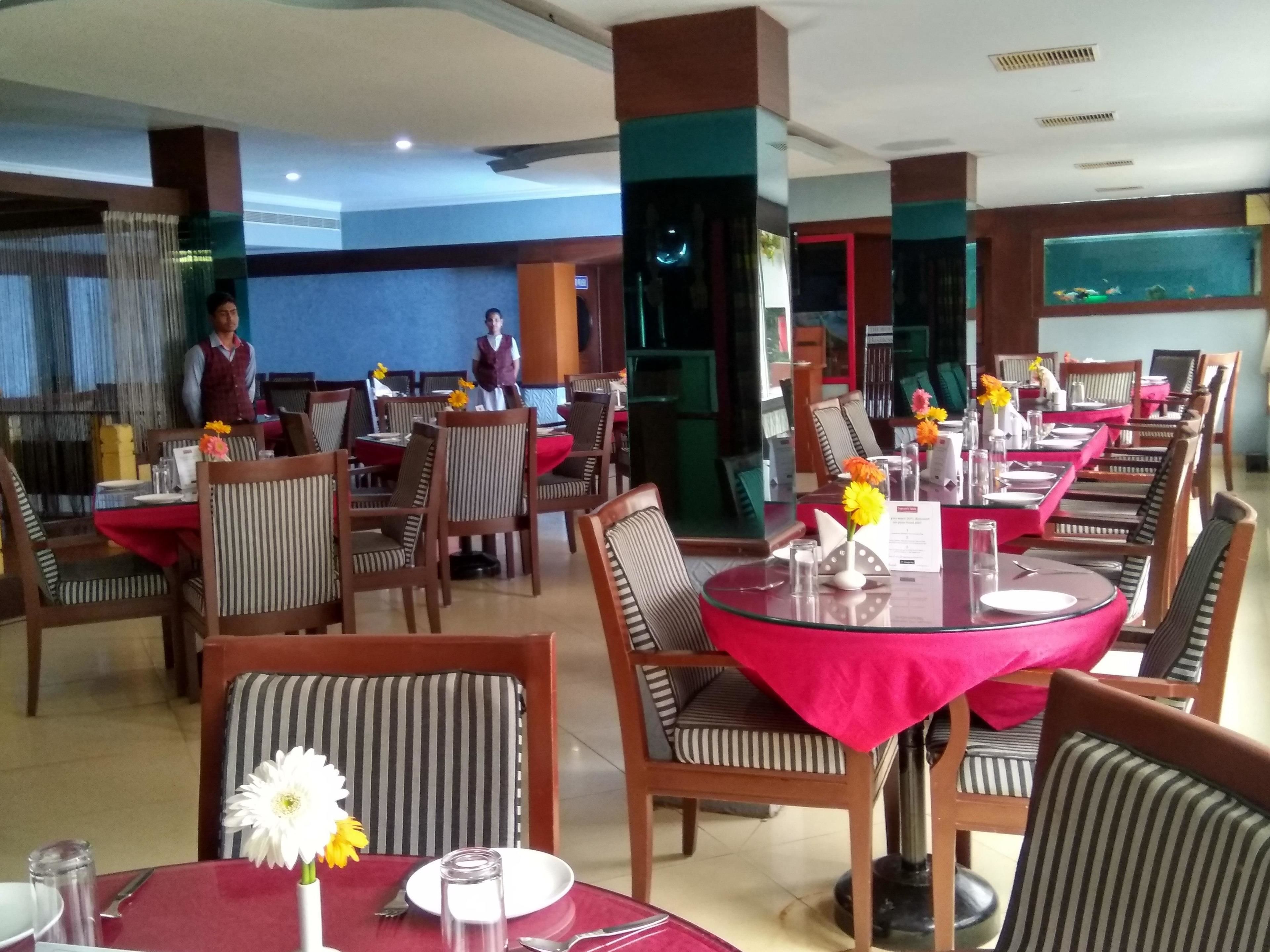 Un restaurante con mesas redondas, sillas a rayas y manteles rojos.