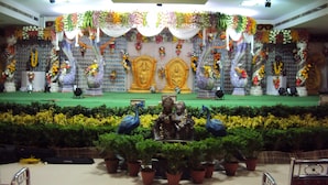 A stage with a floral backdrop, statues, and a green carpet.