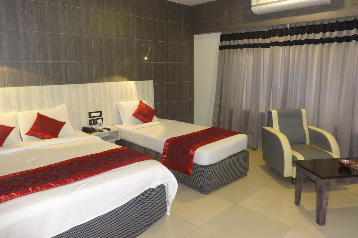Een hotelkamer met twee bedden, een stoel, een tafel, een airconditioner en een plafondventilator.