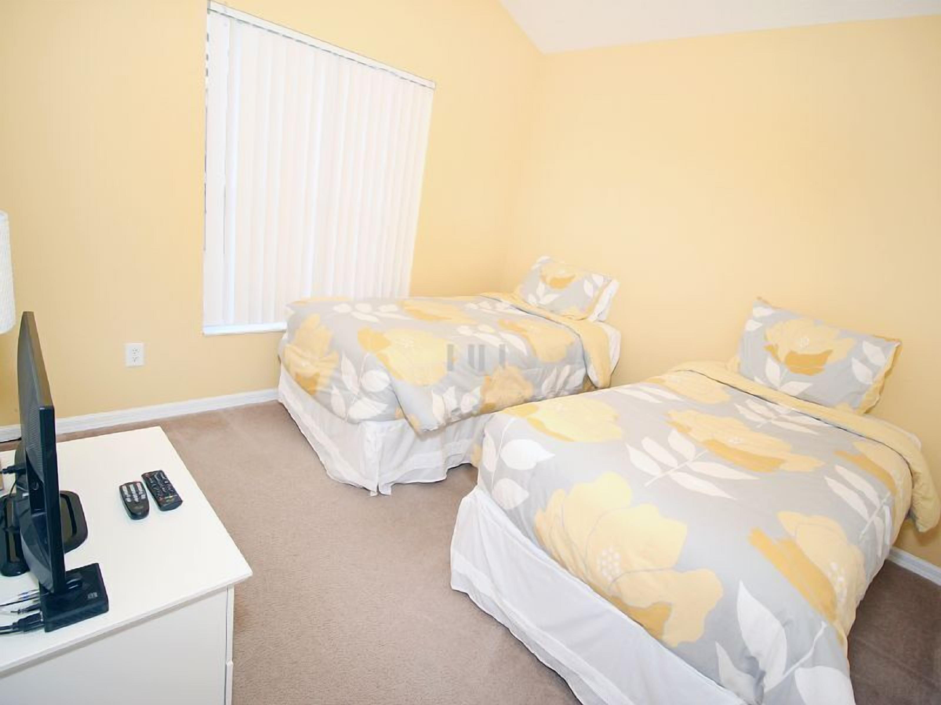 A bedroom with two beds, a TV, and remote controls on a desk.