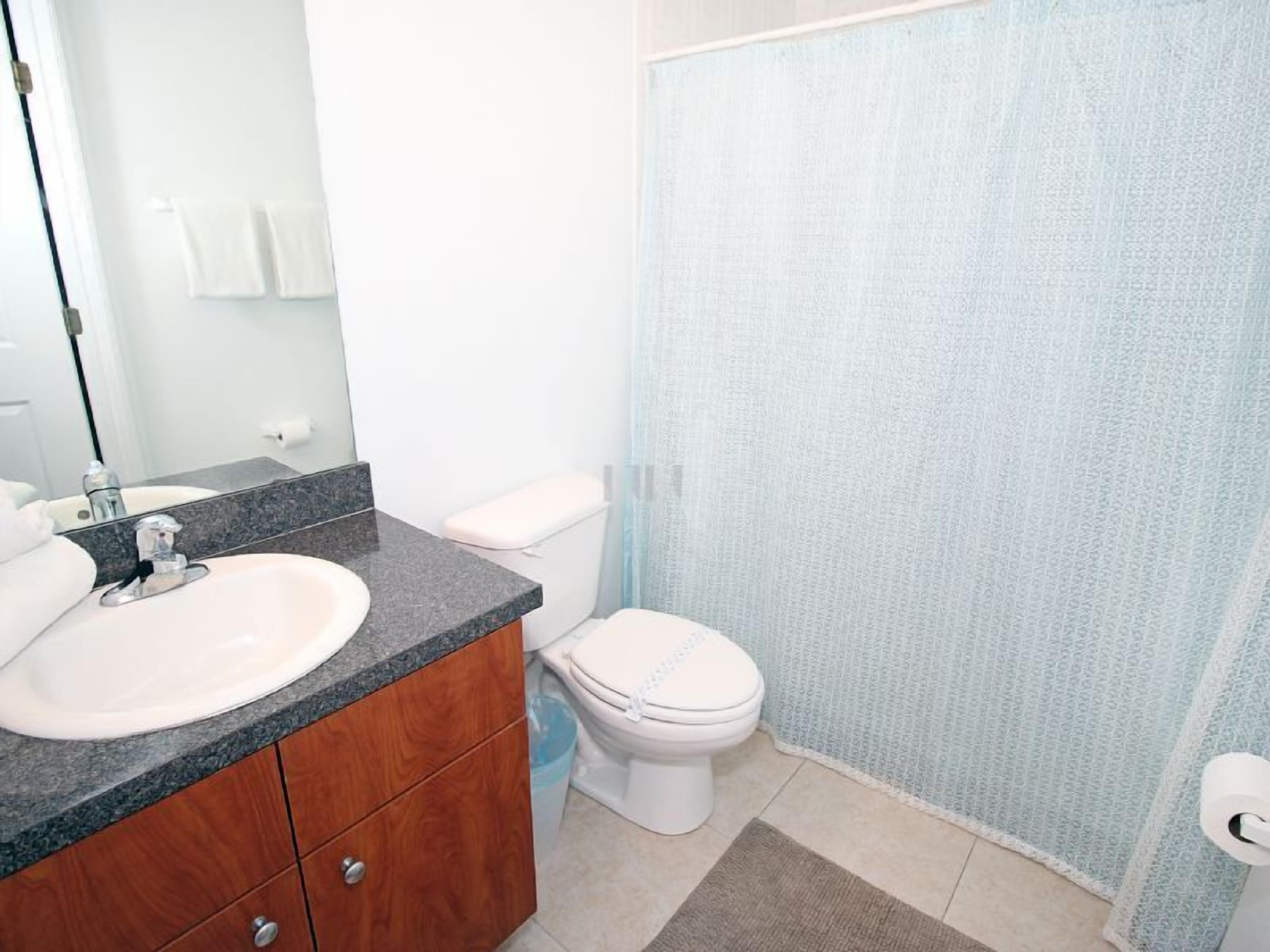 A bathroom with a sink, mirror, toilet, and shower curtain.