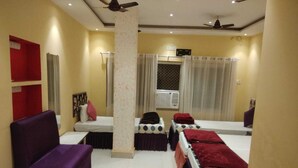 A hotel room with a bed, a sofa, a small table, a mirror, and a window with curtains. - Hotel Samman (Varanasi)