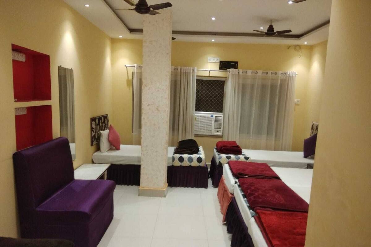 A hotel room with a bed, a sofa, a small table, a mirror, and a window with curtains.