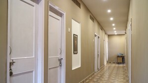 A hallway with white doors, a framed picture on the wall, and a small table at the end. - Hotel Samman (Varanasi)