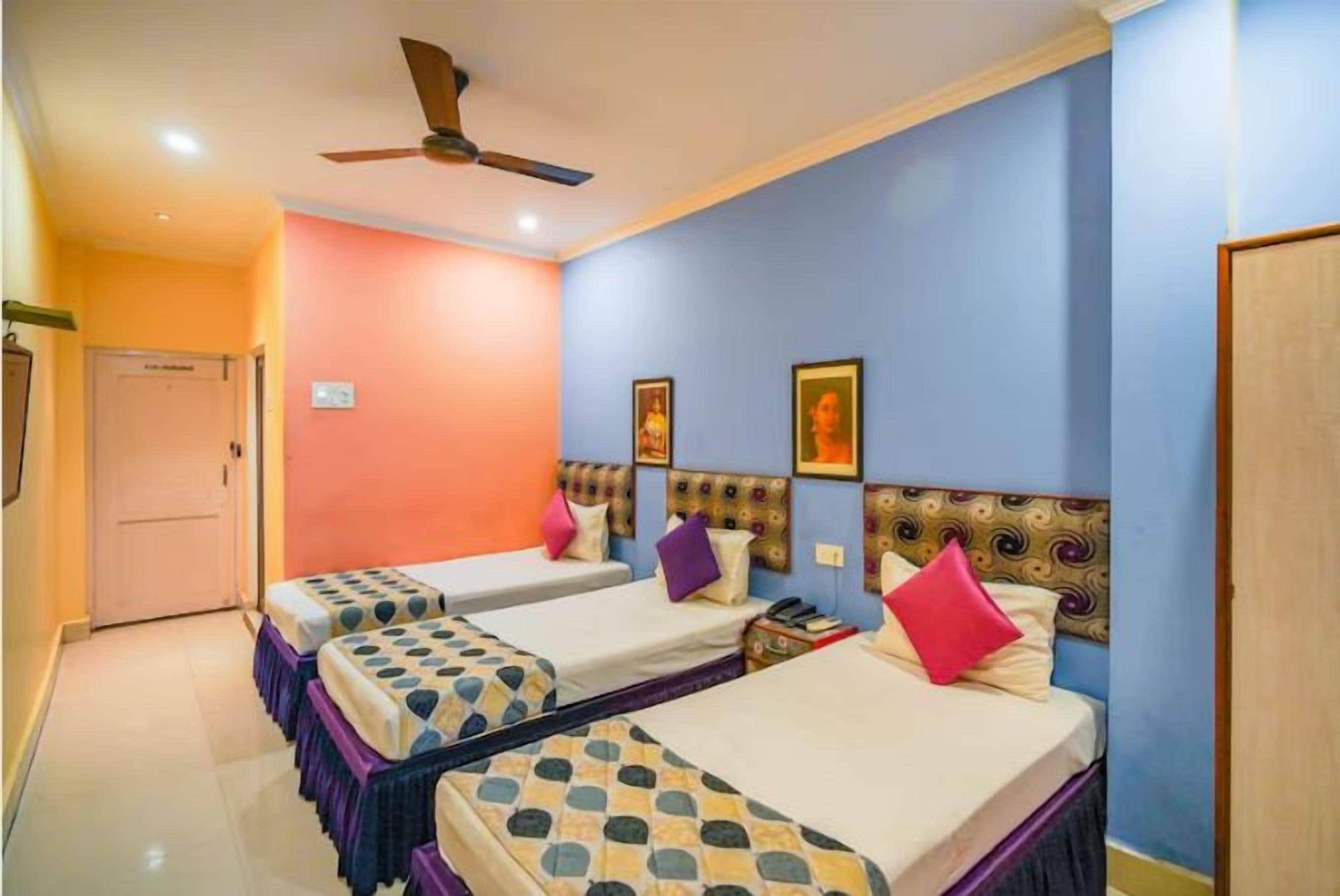 Habitación de hotel con tres camas individuales, un ventilador de techo y una puerta.